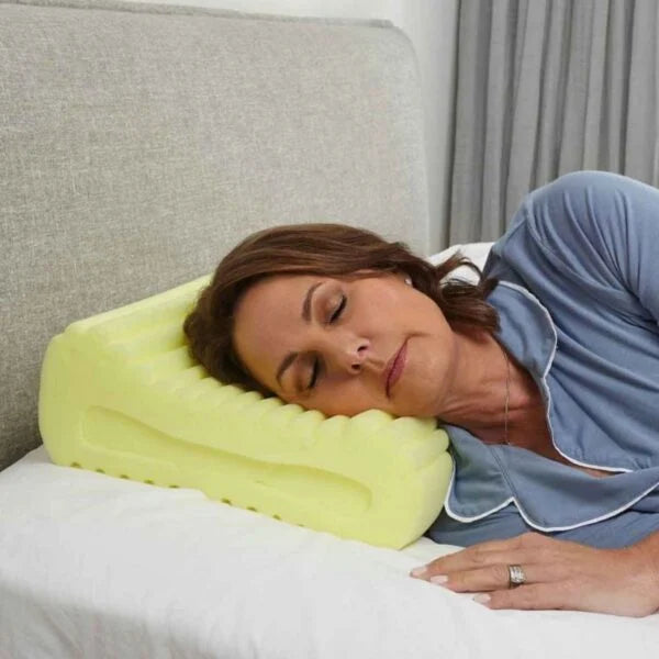 Woman lying on a bed with a sleeprrr therapeutic memory foam pillow, wearing a blue shirt.